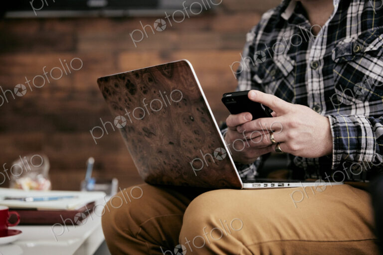 Man using a mobile phone and balancing his laptop on his knee.