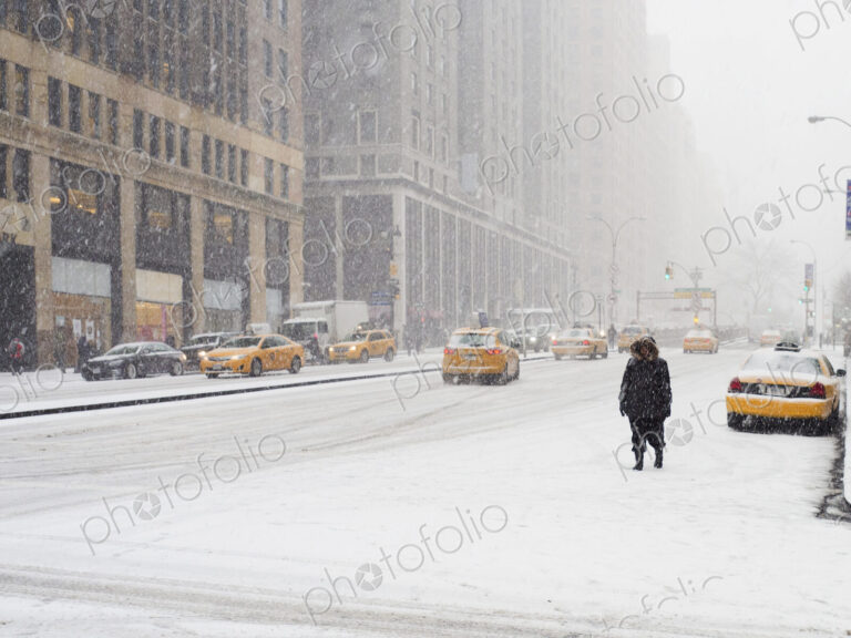 Man walking in a city in the snow during a blizzard, yellow taxis on the street.