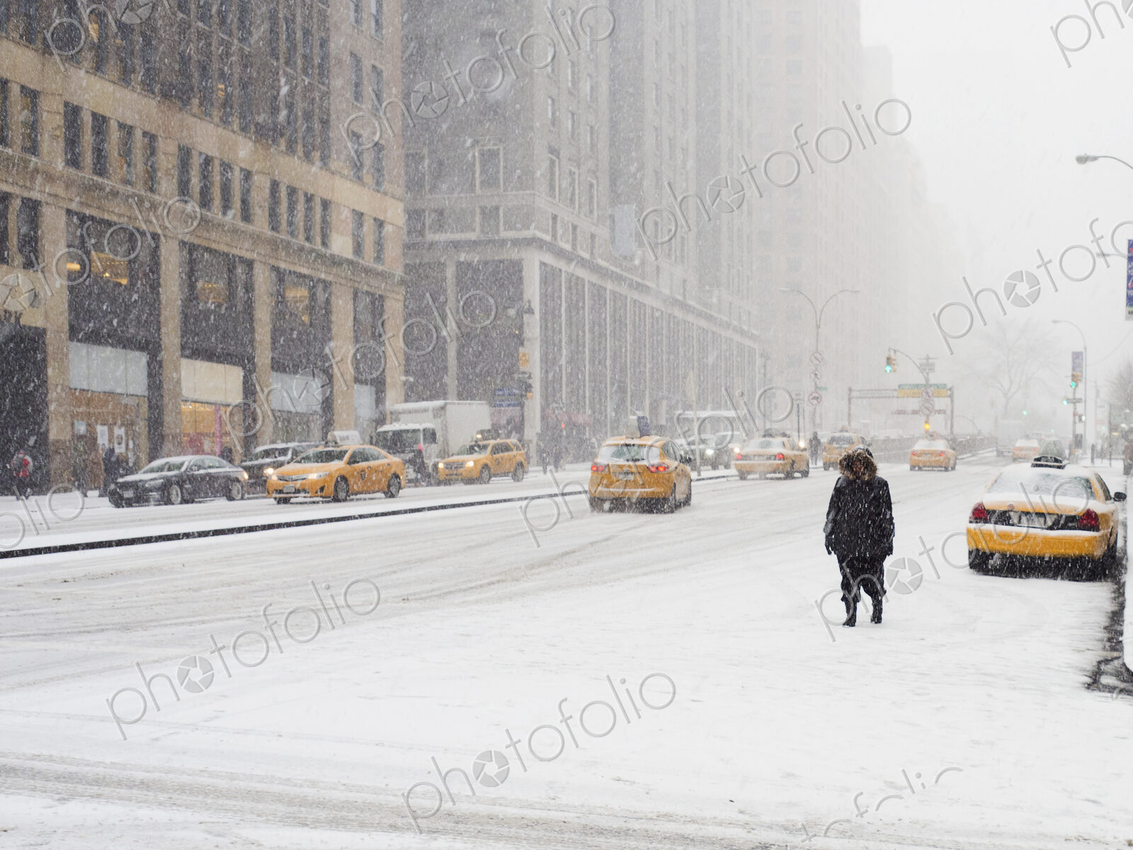 Man walking in a city in the snow during a blizzard, yellow taxis on the street.