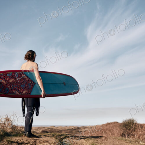 Man walking on a path in the sand dunes towards sea carrying a surf board. Man walking on a path in the sand dunes towards sea carrying a surf board.