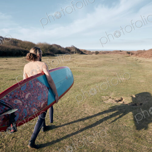Man walking on a path in the sand dunes towards sea with a surf board Man walking on a path in the sand dunes towards sea with a surf board