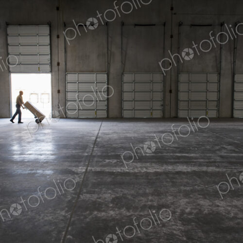 Man walking with loaded hand truck past loading dock doors in new empty warehouse. Man walking with loaded hand truck past loading dock doors in new empty warehouse.