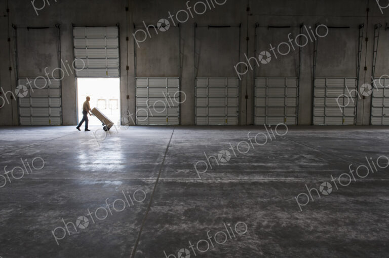 Man walking with loaded hand truck past loading dock doors in new empty warehouse.