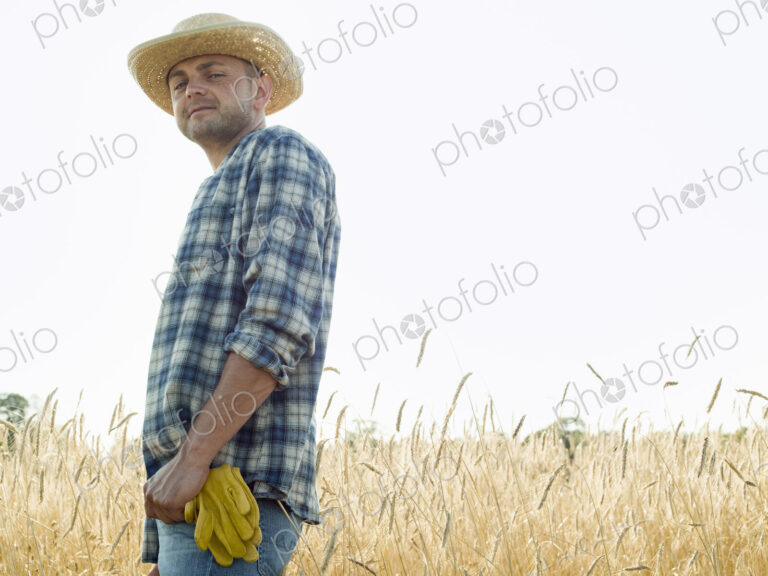 Man wearing a checked shirt and a hat in a cornfield.