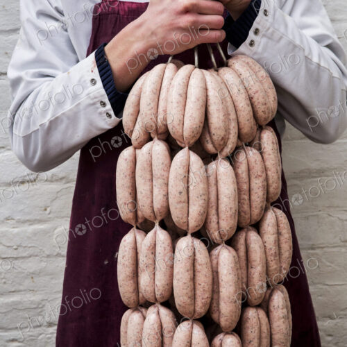 Man wearing apron holding large number of freshly made sausages hanging from hooks. Man wearing apron holding large number of freshly made sausages hanging from hooks.