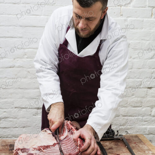 Man wearing apron standing at a wooden butcher's block, butchering piece of pork loin.