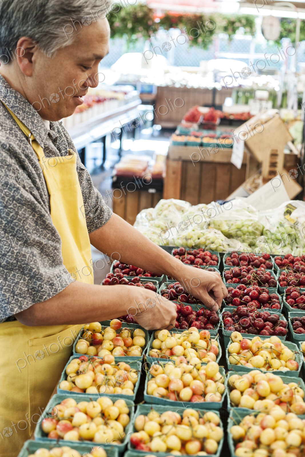 Man wearing apron standing at stall with punnets of fresh cherries at a fruit and…