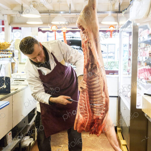 Man wearing apron standing in butcher shop, butchering half a pig.