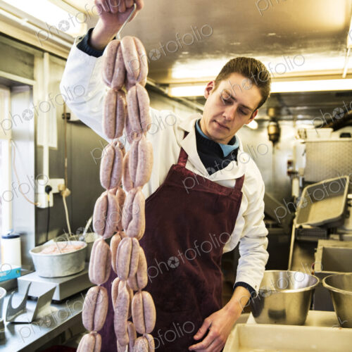 Man wearing apron standing in butcher shop, holding large number of freshly made… Man wearing apron standing in butcher shop, holding large number of freshly made…