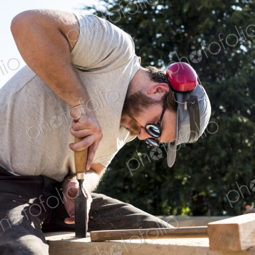 Man wearing baseball cap, sunglasses and ear protectors on building site, working on…