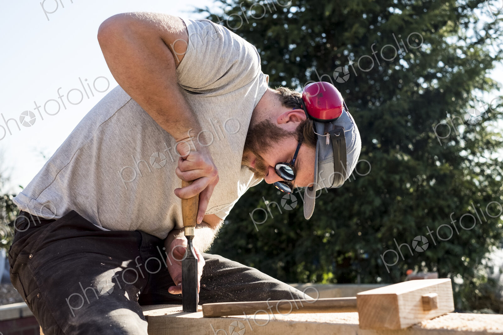 Man wearing baseball cap, sunglasses and ear protectors on building site, working on…