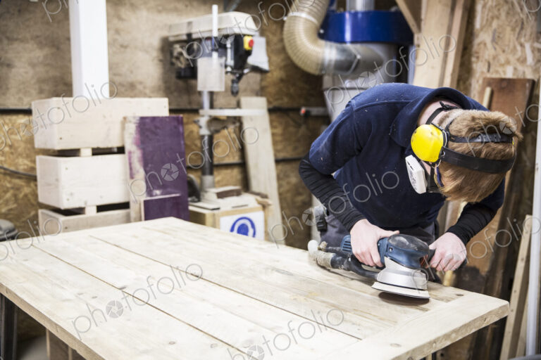 Man wearing ear protectors, protective goggles and dust mask standing in a warehouse,…