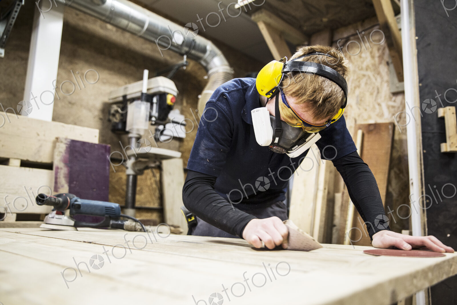 Man wearing ear protectors, protective goggles and dust mask standing in a warehouse,…