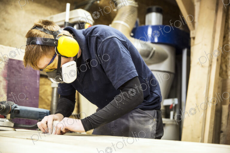 Man wearing ear protectors, protective goggles and dust mask standing in a warehouse,…