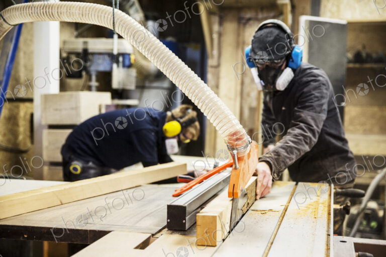 Man wearing ear protectors, protective goggles and dust mask standing in a warehouse,…