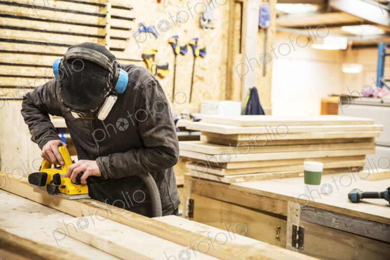 Man wearing ear protectors, protective goggles and dust mask standing in a warehouse,…