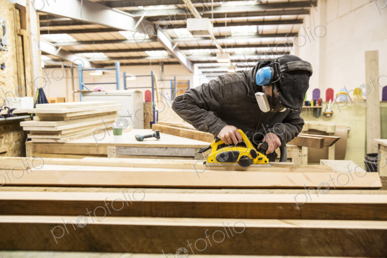 Man wearing ear protectors, protective goggles and dust mask standing in a warehouse,…