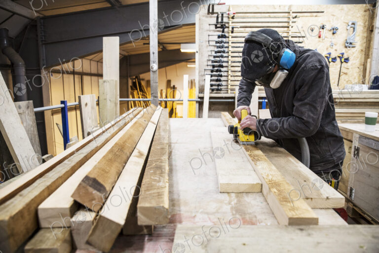 Man wearing ear protectors, protective goggles and dust mask standing in a warehouse,…