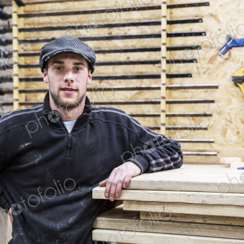 Man wearing flat cap standing next to a stack of wooden boards, looking at camera,… Man wearing flat cap standing next to a stack of wooden boards, looking at camera,…