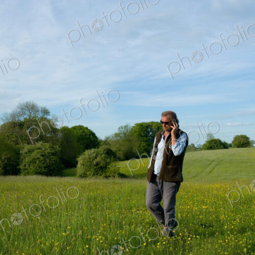 Man wearing sunglasses walking across meadow, holding mobile phone to his ear. Man wearing sunglasses walking across meadow, holding mobile phone to his ear.