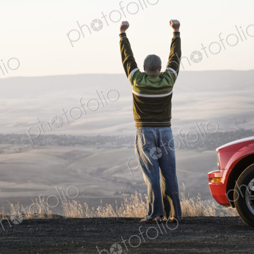Man with arms in the air standing next to his car at a rest stop on a highway Man with arms in the air standing next to his car at a rest stop on a highway