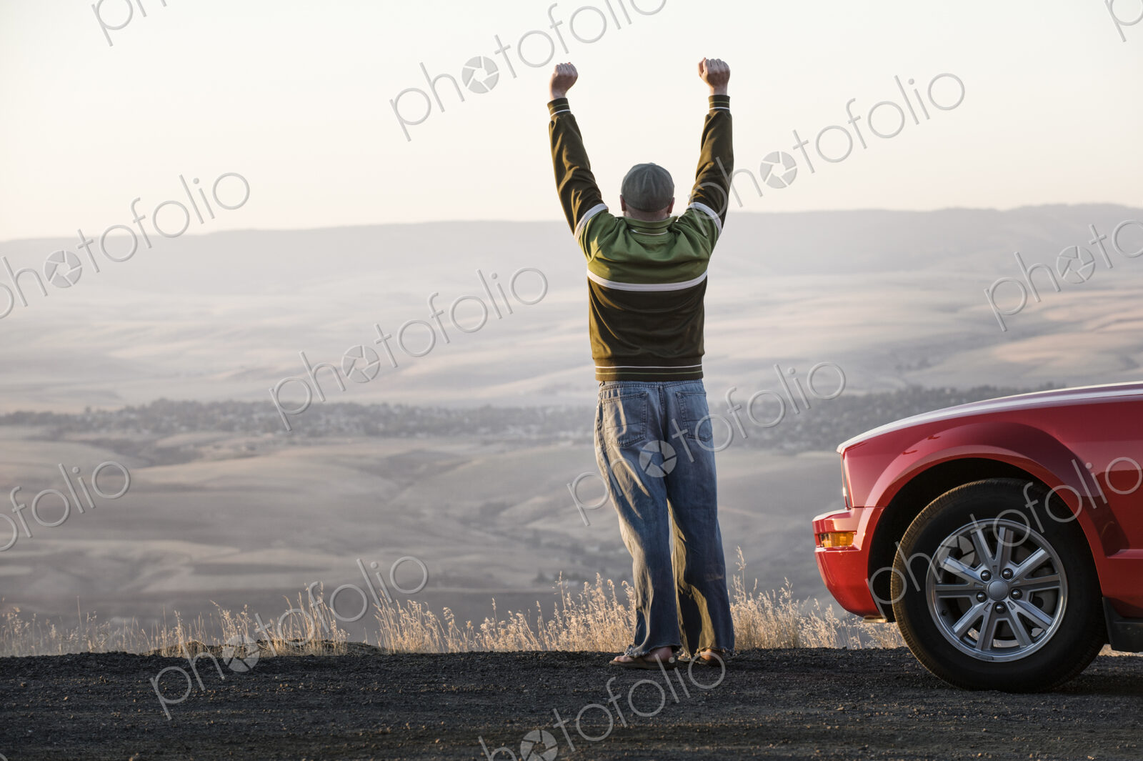 Man with arms in the air standing next to his car at a rest stop on a highway