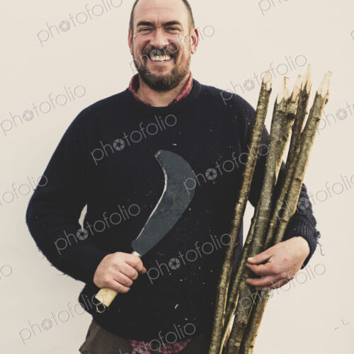 Man with bill hook and bunch of wooden stakes for traditional hedge laying