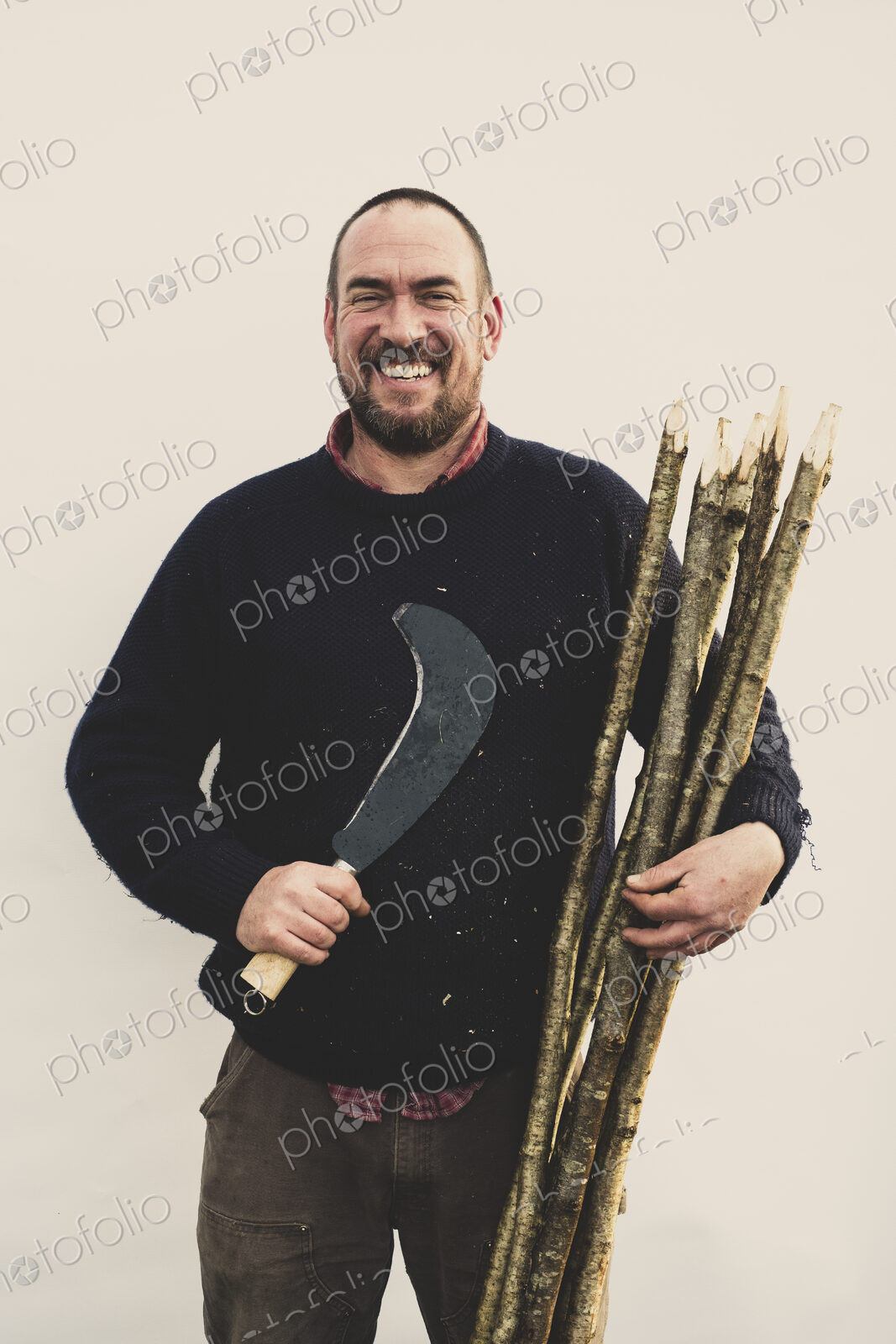 Man with bill hook and bunch of wooden stakes for traditional hedge laying