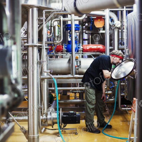 Man working in a brewery adjusting and checking the machinery which transfers the… Man working in a brewery adjusting and checking the machinery which transfers the…