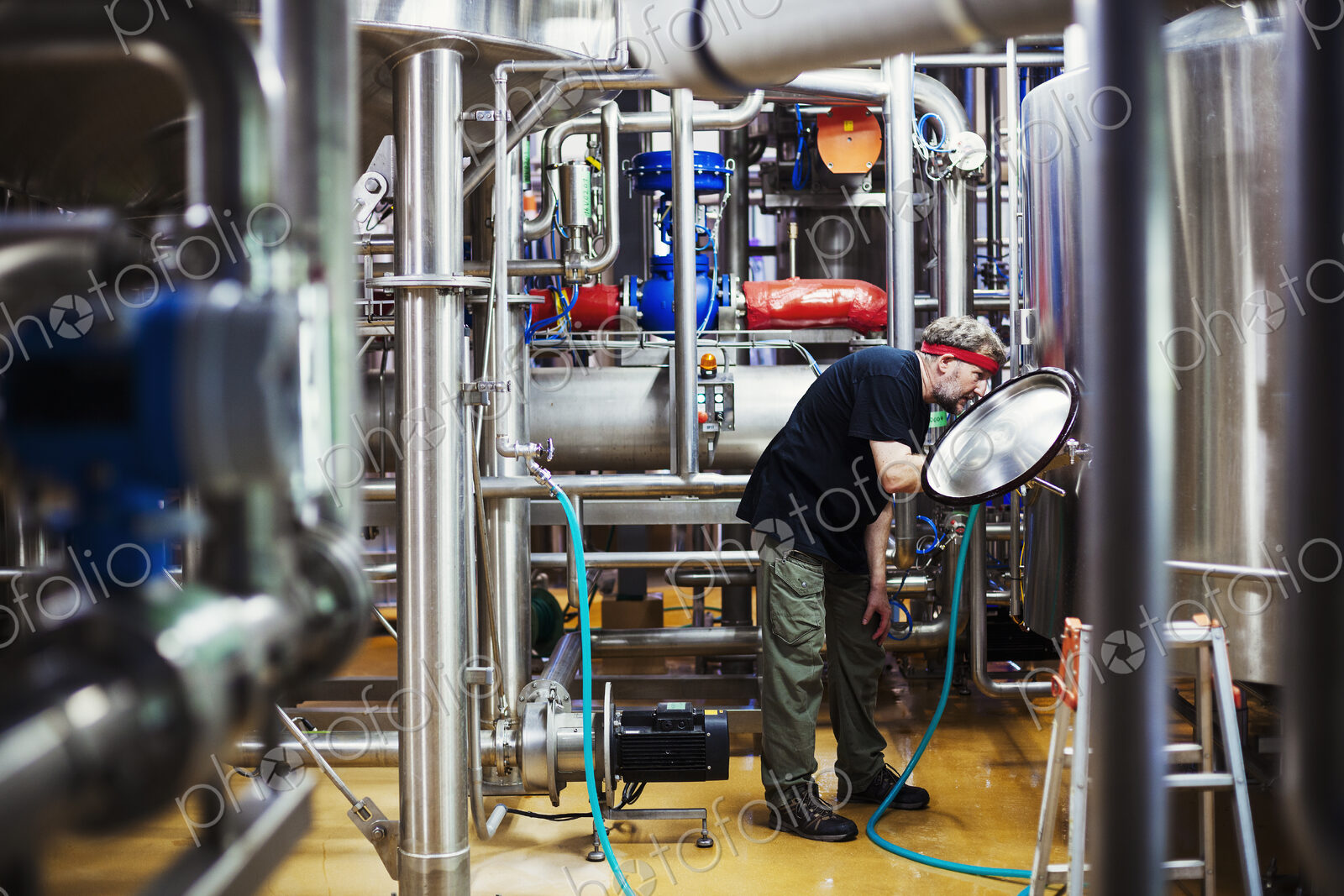 Man working in a brewery adjusting and checking the machinery which transfers the…