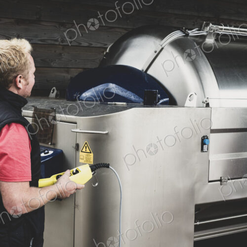 Man working on a vineyard, standing next to large stainless steel tank.
