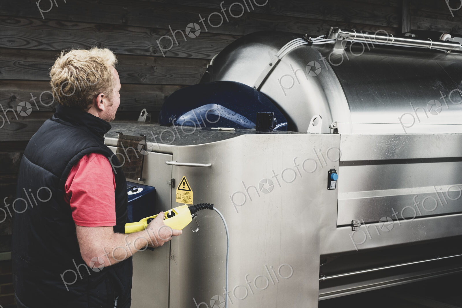 Man working on a vineyard, standing next to large stainless steel tank.