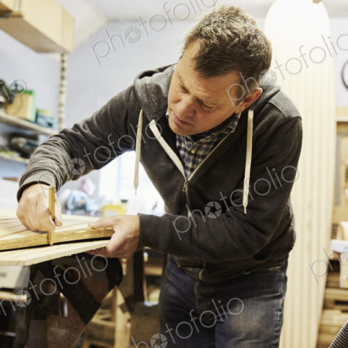 Man working on the edge of a wooden shaped board in a woodwork shop.