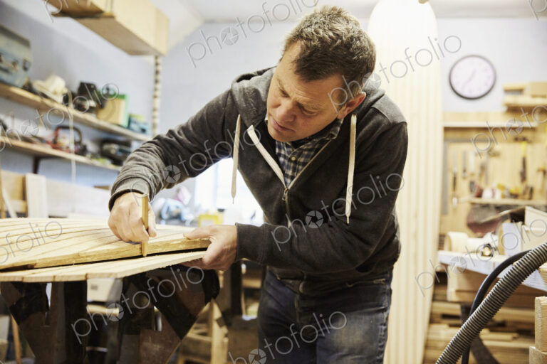 Man working on the edge of a wooden shaped board in a woodwork shop.