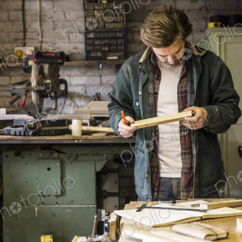 Man working standing at a workbench in a woodworking workshop, holding piece of wood.