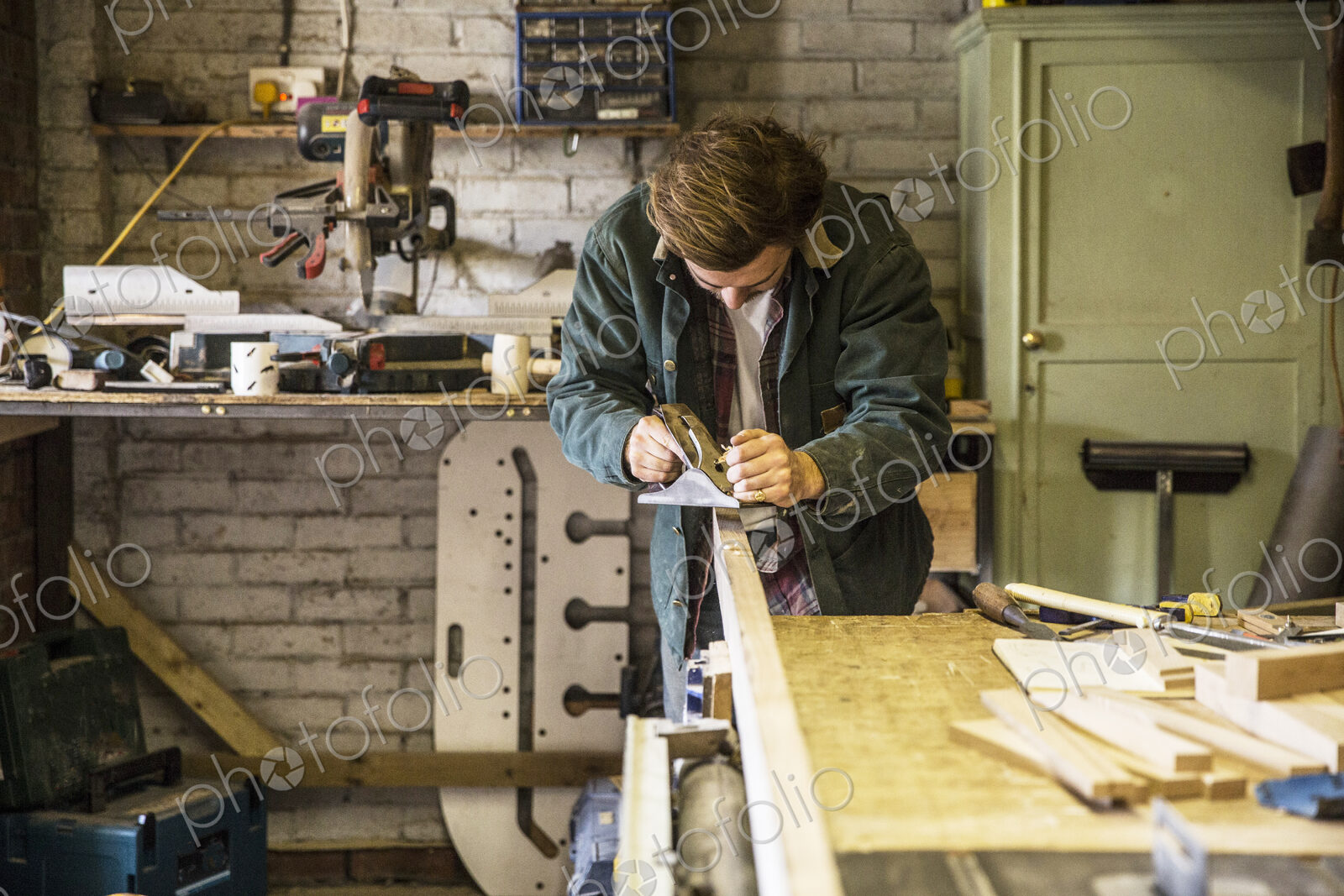 Man working standing at a workbench in a woodworking workshop, using plane on plank of…