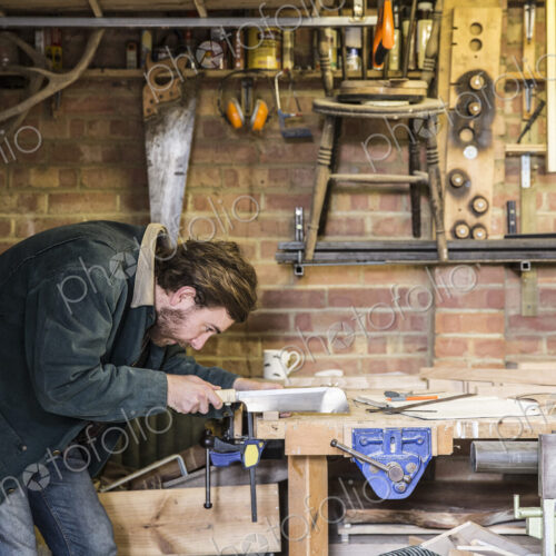 Man working standing at a workbench in a woodworking workshop, using saw on piece of wood. Man working standing at a workbench in a woodworking workshop, using saw on piece of wood.