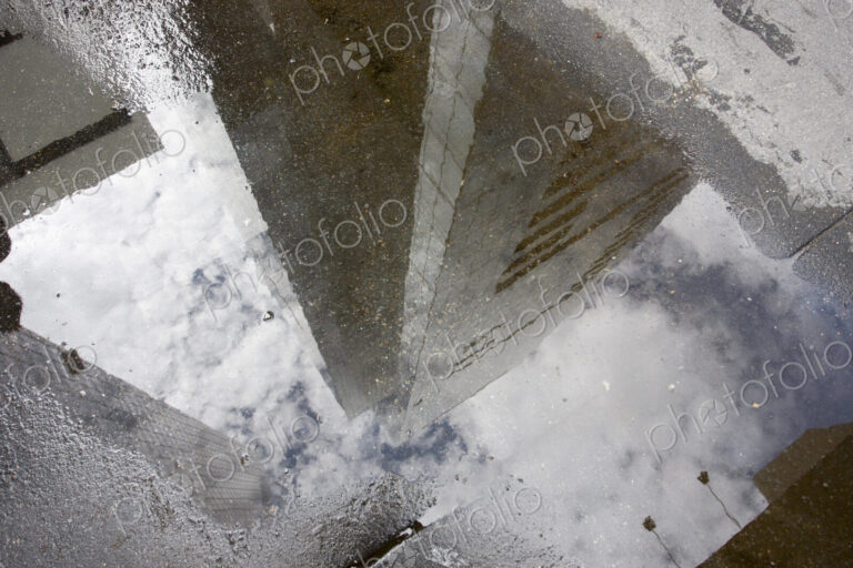 Manhattan skyscrapers reflecting in a rain puddle on the sidewalk.