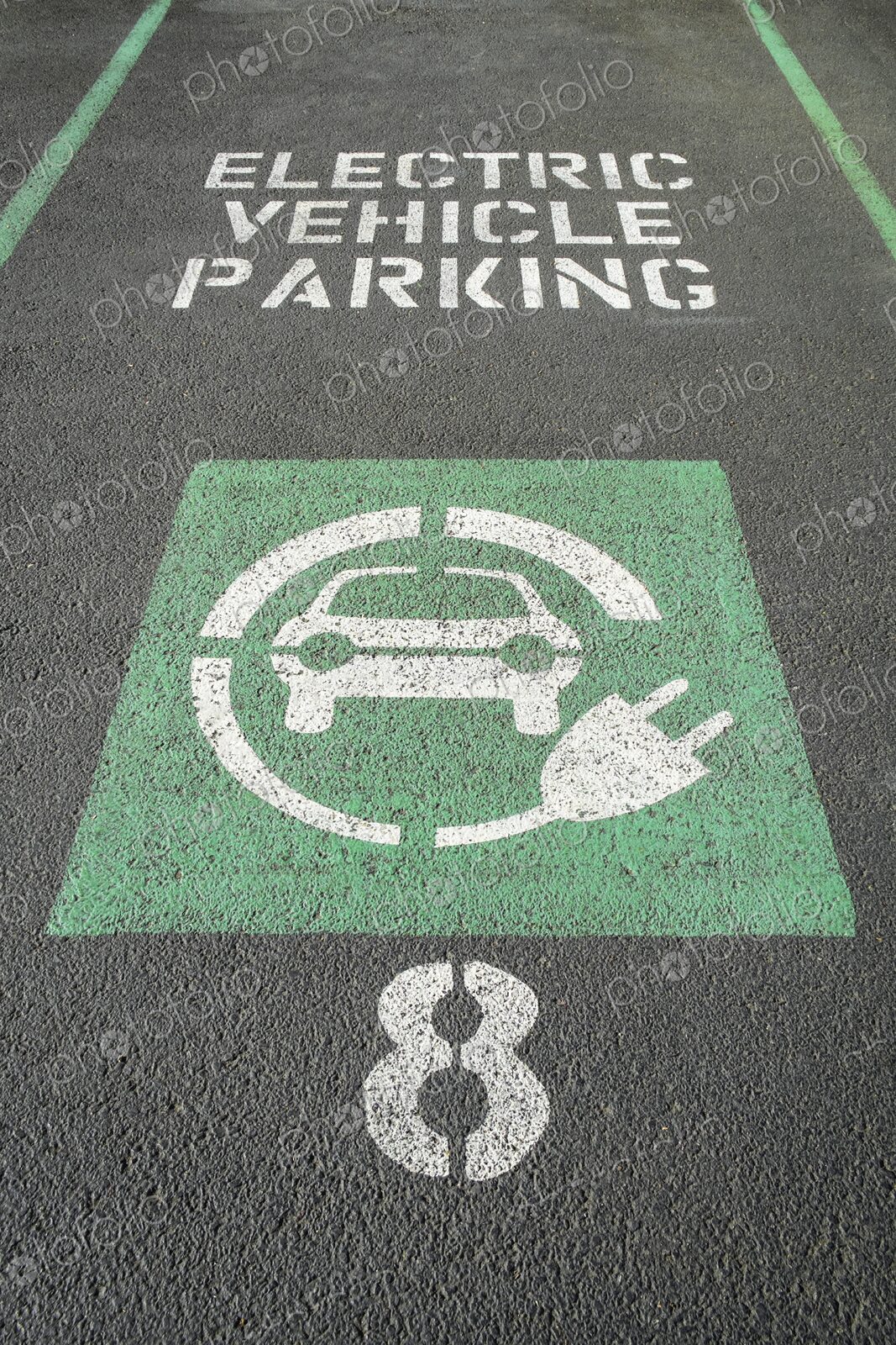 Marked parking space reserved for electric vehicles with green EV symbol and charging…