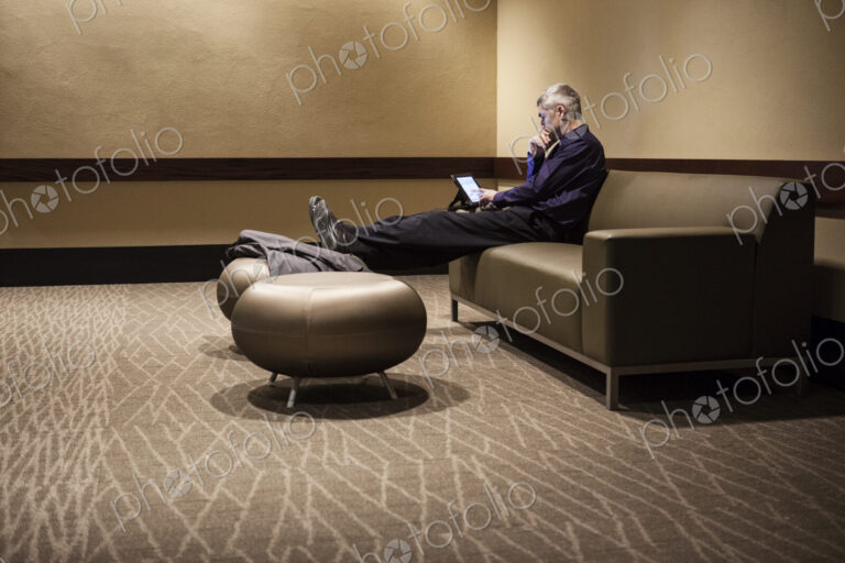 Mature businessman with his feet up, resting in an armchair, looking at his mobile phone.