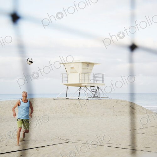 Mature man standing on a beach, playing beach volleyball.