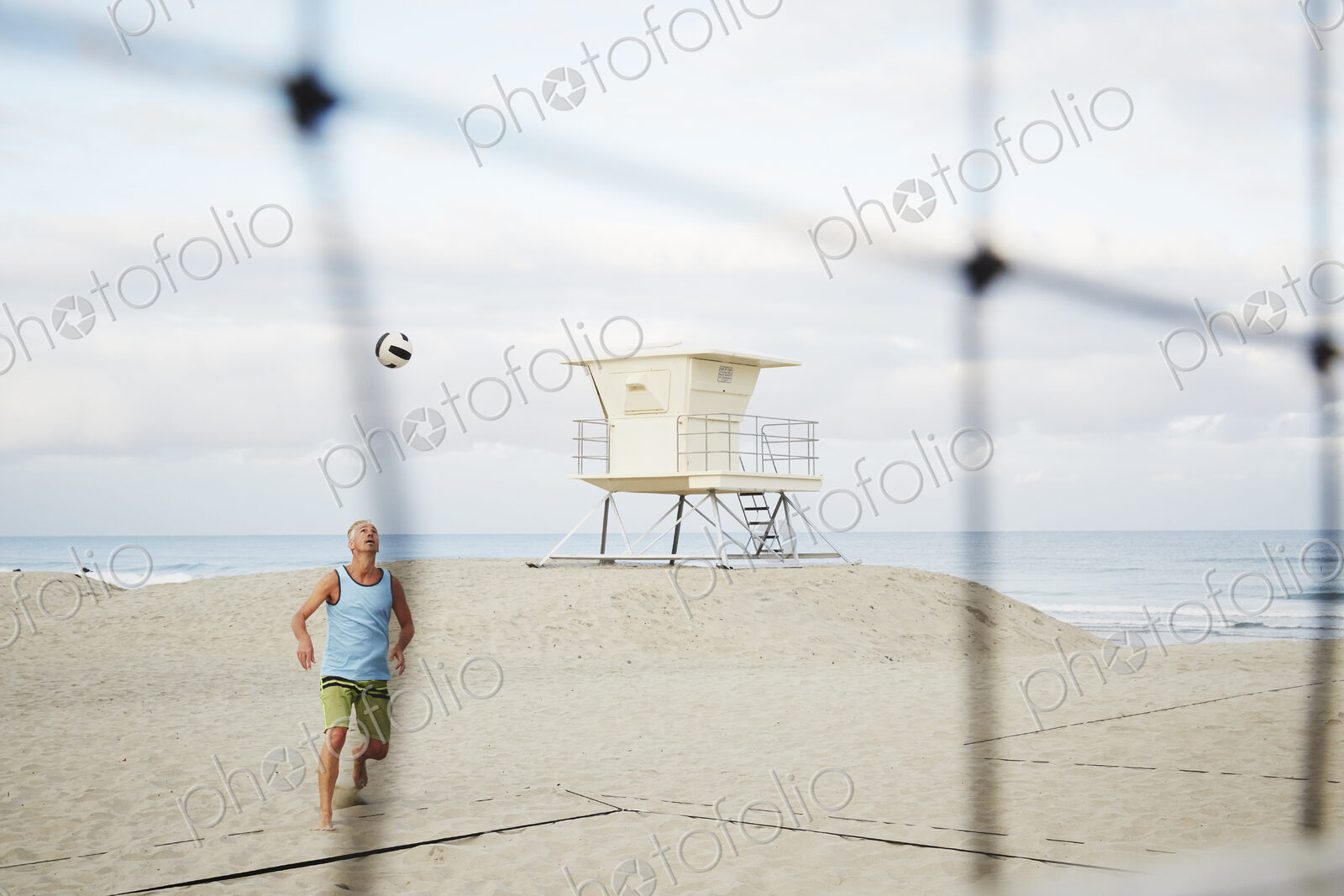 Mature man standing on a beach, playing beach volleyball.