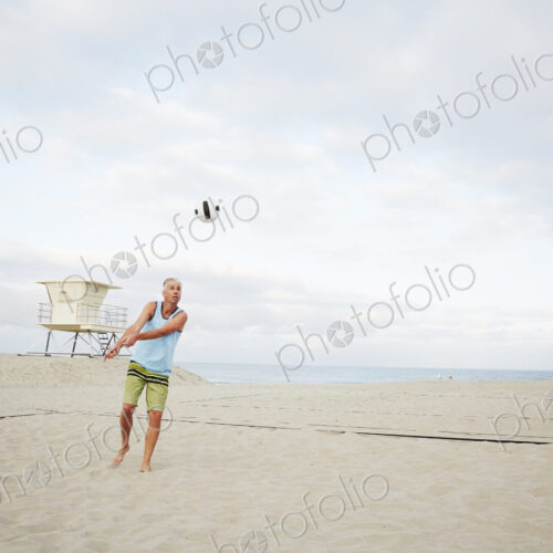 Mature man standing on a beach, playing beach volleyball.