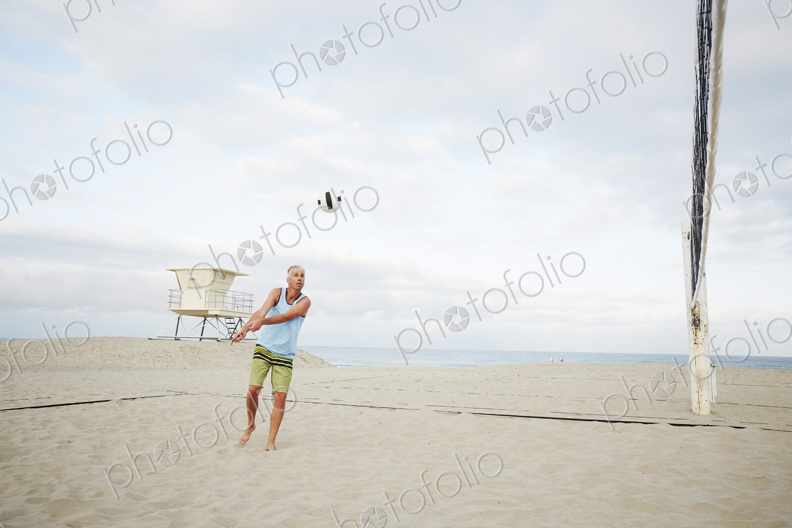 Mature man standing on a beach, playing beach volleyball.
