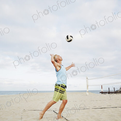 Mature man standing on a beach, playing beach volleyball.