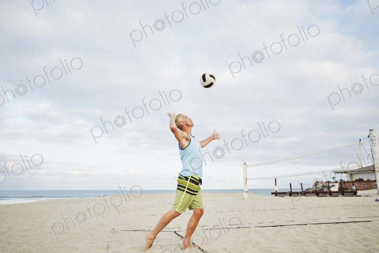 Mature man standing on a beach, playing beach volleyball.