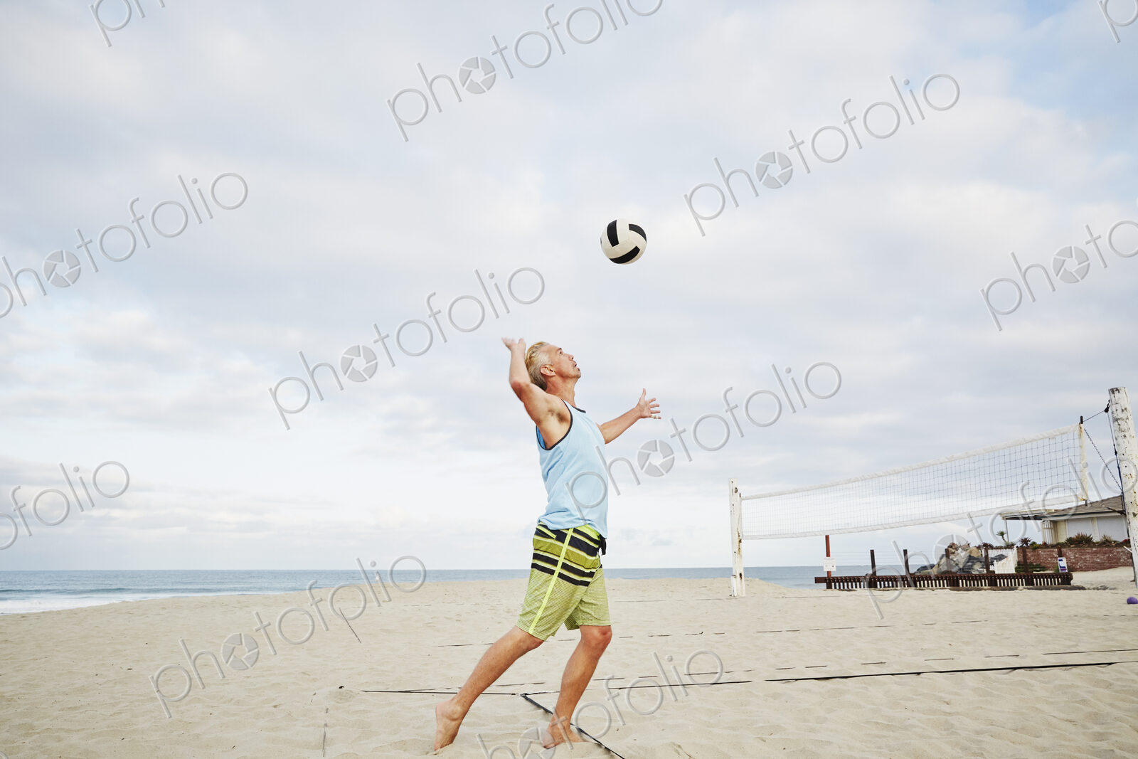 Mature man standing on a beach, playing beach volleyball.