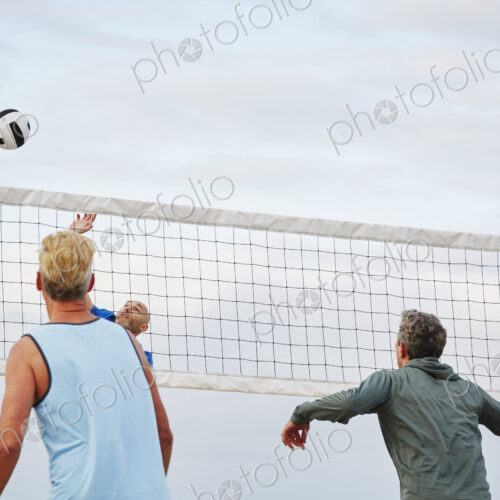 Mature men standing on a beach, playing beach volleyball.