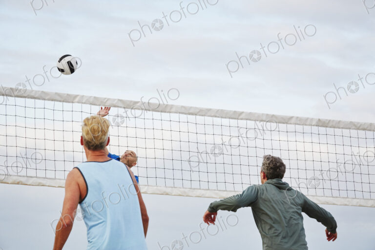 Mature men standing on a beach, playing beach volleyball.