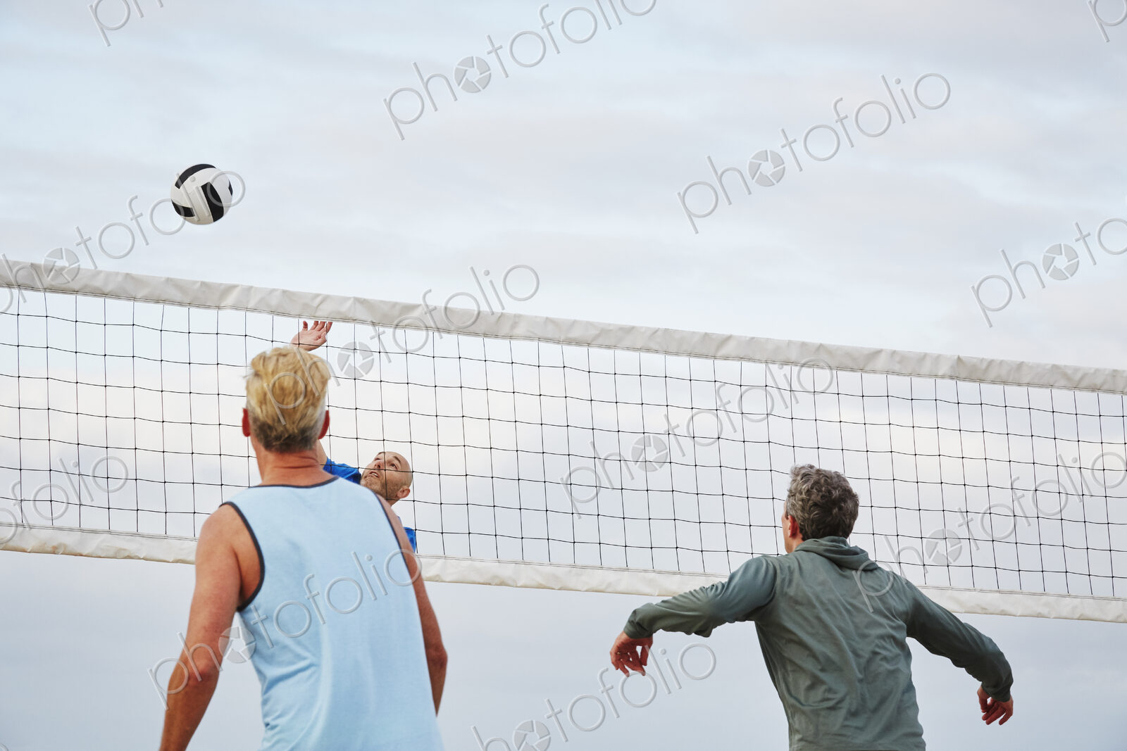 Mature men standing on a beach, playing beach volleyball.